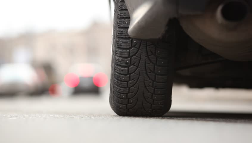 Rear tyre of starting car, vehicle begin to move, environment road noise. Low camera position, studded tire of standing car. Left rear wheel view, auto ride away, rendered in blur at distance. Royalty-Free Stock Footage #19300894
