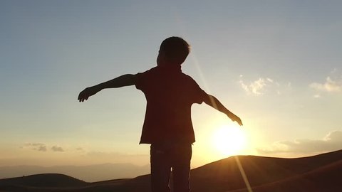 SLOW MOTION: Kid silouette spreading arms and looking to the infinite at the sunset. Conceptual footage.
