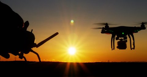 Person operating drone quadcopter aircraft via remote control at sunset