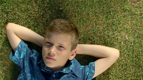 Portrait of a teenage boy lying in the grass. Child relaxing in a field in spring, summer.