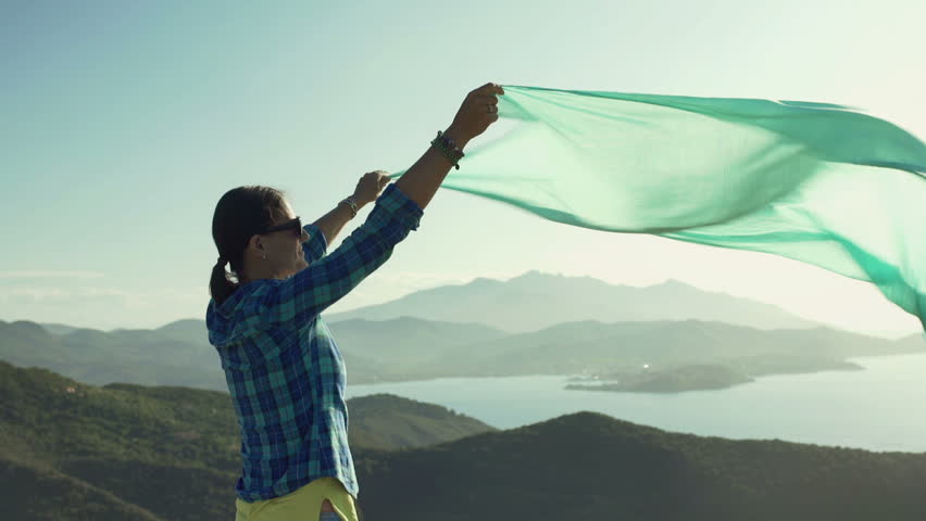 Happy woman holding blue scarf which is moving on the wind, steadycam shot
