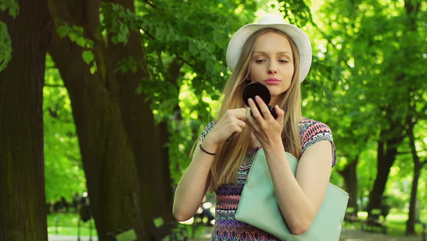 Stylish girl looking to the mirror and checking her appearance in the park

