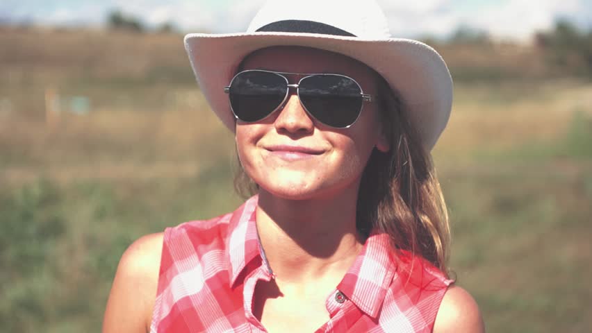 Young american cowgirl woman portrait outdoors. Beautiful natural woman smiling and looking at camera touching cowboy hat.