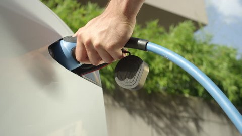 CLOSE UP, SLOW MOTION: Man plugging in electric car at home at electro charging station. Luxury white electrical car recharging. Environmentally conscious man charging his electric vehicle