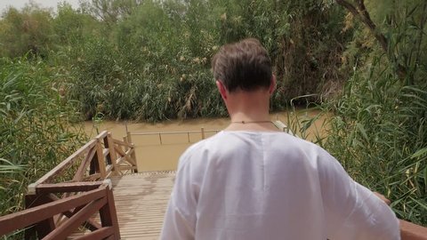 Man is Walking Downstairs to Jordan River, Israel. Small Swampy River. Worshiper in White Long Shirt is Going to Immerse ti a Water. Man is Walking Foreward With His Back to Camera. Wooden Stairs