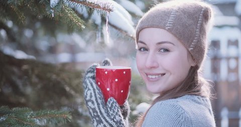 Woman Drinks Hot Tea or Coffee From a Cozy Cup on Snowy Winter Morning Outdoors. 4K DCi SLOW MOTION 120 fps. Beautiful Girl Enjoying Winter in a Garden with a Mug of Warm Drink. Christmas Holidays 