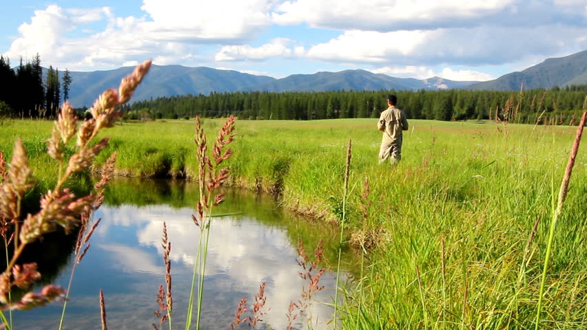 Man casting his fishing pole into a sunny creek on a grassy ranch in Montana