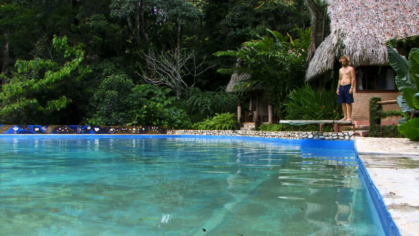 Man diving into a pool in front of a hut and lush jungle