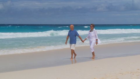 camera following senior couple walking on the beach