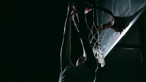 Low angle of reverse dunk performing by professional basketball player in dark court in slow motion