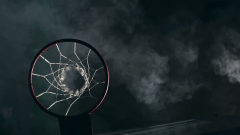 Top view of two basketball opponents jumping in the air and one man slamming ball in the net in the dark court with smoke in slow motion