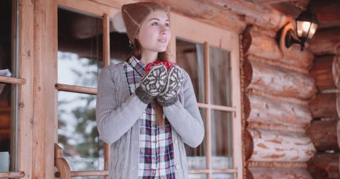 Woman with Cup of Hot Tea or Coffee Walks out the Cozy House on Snowy Winter Morning. 4K DCi SLOW MOTION 120 fps. Beautiful Girl Enjoying Winter Outdoors with a Mug of Warm Drink. Christmas Holidays 
