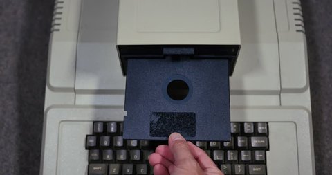Overhead shot of someone inserting and removing an old-style 5.25-inch floppy disk. Shallow depth of field.	 	