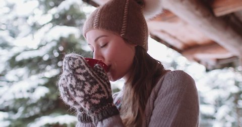 Woman Drinks Hot Tea or Coffee From Cup at Cozy Snowy House Garden on Winter Morning. 4K DCi SLOW MOTION 120 fps. Beautiful Girl Enjoying Winter Outdoors with a Mug of Warm Drink. Christmas Holidays 