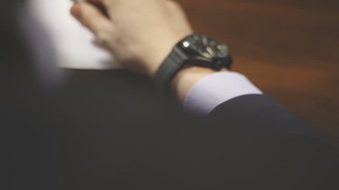 Businessman checking wrist watch. The watch on the hand. The man in the jacket looks at his watch. Businessman sitting at a desk for hours. Business meeting. Attributes businessman. Men's Accessories