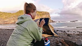 Independent traveler woman using tablet device next to yellow tent with camping gear on an epic camping adventure.