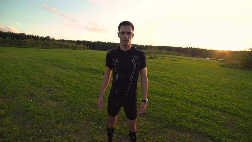 Young athlete doing exercises in beautiful meadow at sunset. Moving the camera. 4K