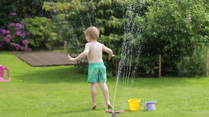 Happy little boy playing and splashing with a garden sprinkler on hot and s...