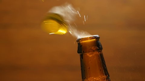 Opening cold bottle of beer with steam and spray (close-up)
