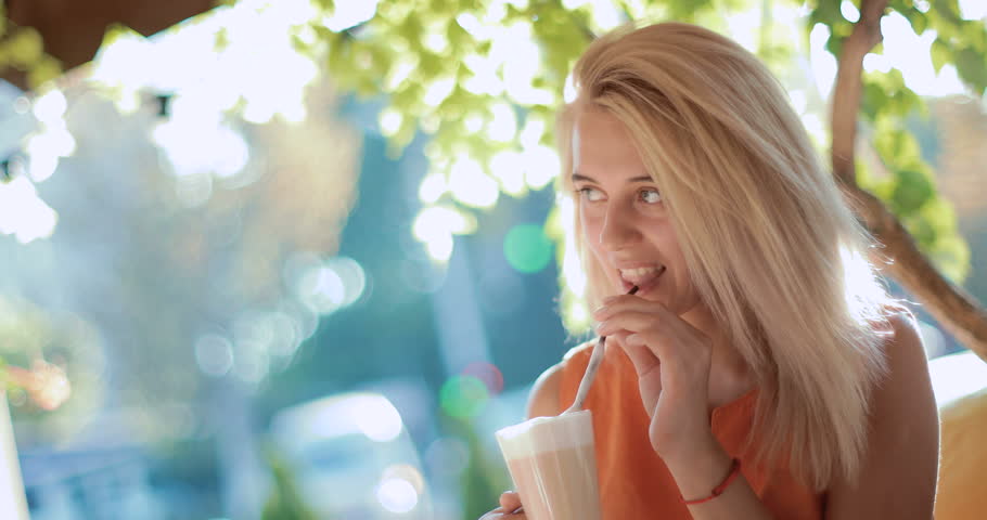 Young, beautiful woman sitting in a restaurant enjoying a cool drink. Beauty smiling and looking very happy and pleased with herself. in slow motion