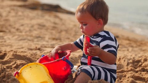 A little toddler boy plays on the sandy ocean beach with his sand toys next to the water