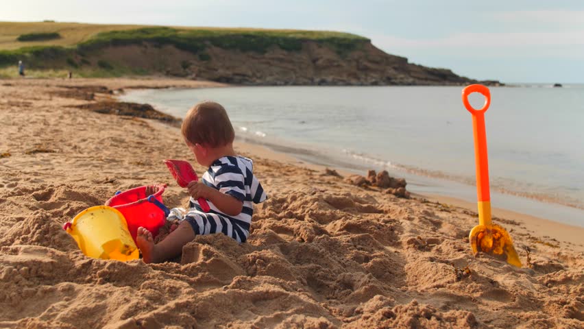 A little toddler boy plays on the sandy ocean beach with his sand toys next to the water