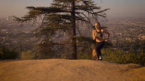 Fit woman Jogging through a park in the Hollywood Hills at sunrise. Hollywood hills and the rising sun can be seen in the background. Slow Motion.