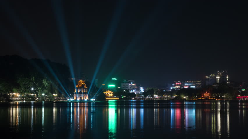 Timelapse shot of Hanoi at night. Illuminated Turtle Tower and Hoan Kiem Lake in city centre. Colorful lights reflecting in dark water, Vietnam