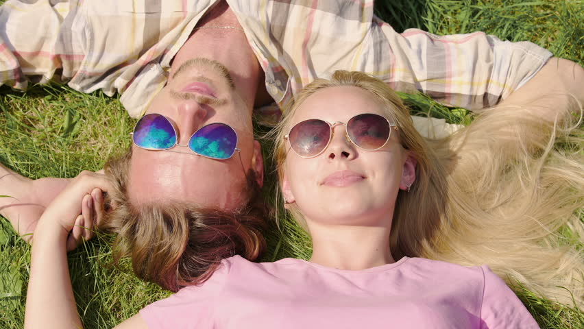 Young happy family lying on grass, kissing, holding hands and enjoying vacation