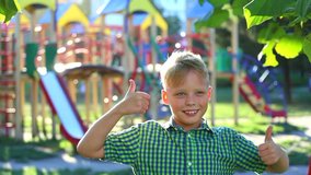 Close up portrait of happy funny cute kid staying in front of camera smiling and laughing. Model released boy poses for camera with thumbs up as sign of like. Real time video footage.
