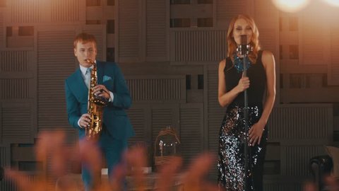 Jazz vocalist in glare dress dance perform with saxophonist in blue suit. Stage. Retro style: stockvideo