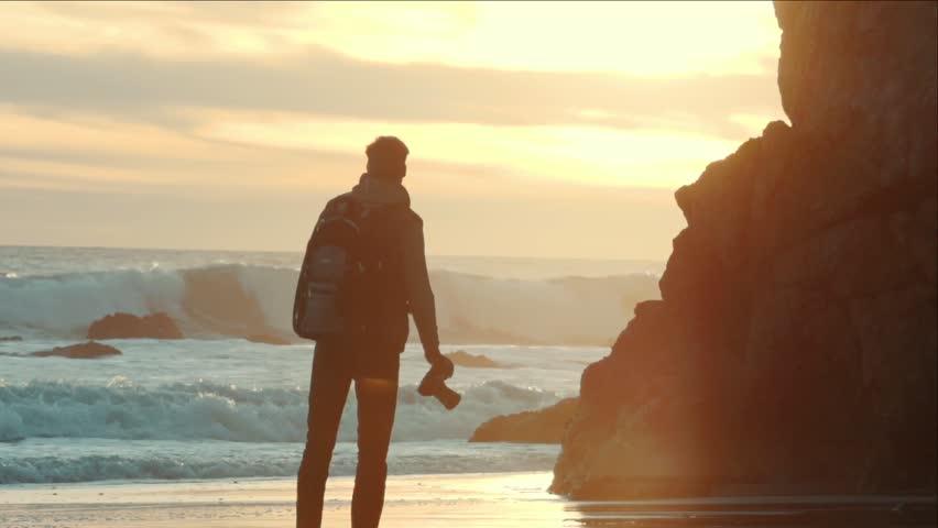 Photographer walks at ocean beach and takes pictures , sunset. Professional camera. / Shot on ARRI ALEXA
