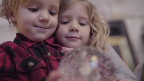 Brother And Sister Curl Up Together And Watch The Snow Settle In A Snow Globe Stockvideó