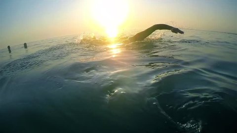 slow motion of professional swimmer swimming crawl outdoor on sunset, back view