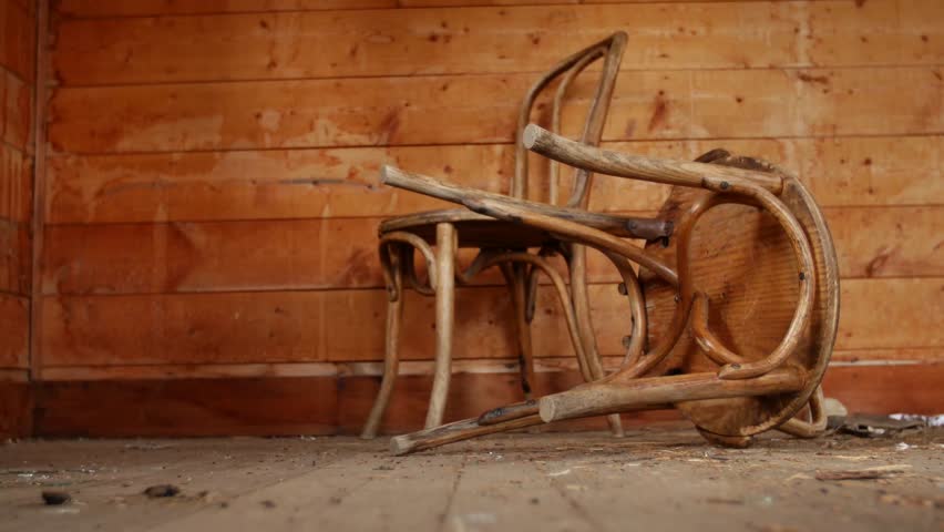 Old wooden chairs sit on the floor of an abandoned wooden cabin.