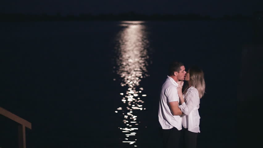 young guy and beautiful girl kissing near the river at night - moonlight