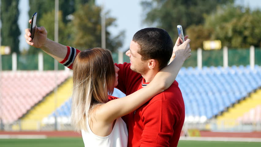young guy and beautiful girl reading a message on your mobile phone - on the football field
