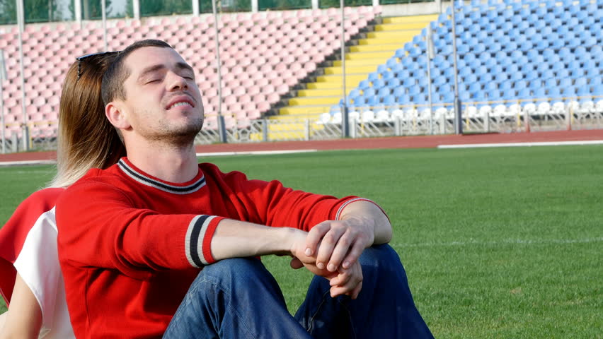 a young man and a beautiful girl at the stadium - are sitting in the middle of the field