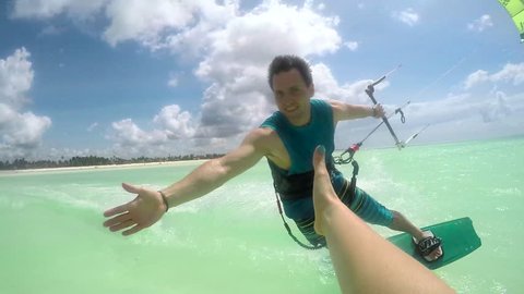 SLOW MOTION: Smiling young kiter kitesurfing and high five slapping in turquoise ocean on sunny day. Cheerful kiteboarder man kiting in beautiful tropical sandy beach lagoon on summer vacation