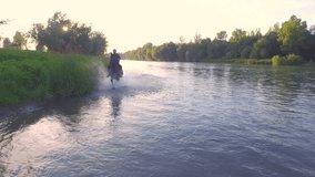 AERIAL CLOSE UP: Flying above horseman horseback riding strong beautiful dark bay gelding trotting in shallow water near grassy riverbank at sunny morning. Senior man on brown horse splashing in river - Powered by Shutterstock - Get 15% off with code: PIKWIZARD15