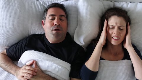 Upset adult woman (female age 30-40) suffering from her partner, a mature adult man (male age 30-40) that snoring during sleep in bed. Couple lifestyle and people health care concept. Copy space