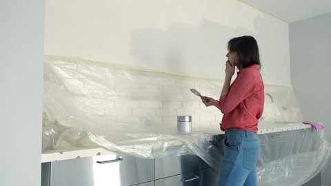 Unhappy woman painting wall in kitchen at her new home
