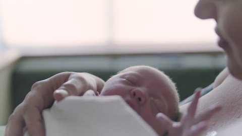 Mother Sitting by Hospital Window Kissing Newborn Baby on Forehead After Birth