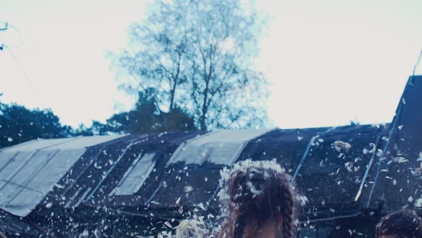 Children and man fight pillows in yard of country house. Many feathers fly. Summer holidays. Fun. Slow motion