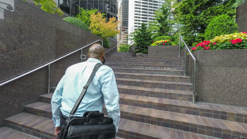 Adult African American businessman walking up steps on his way to work, carrying a laptop case over his shoulder