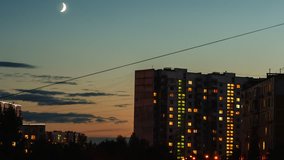 Young moon moving over houses of the big city