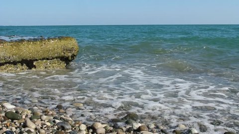Waves beat against the breakwater. Waves washing the pebble beach. Sea waves washes pebble beach.