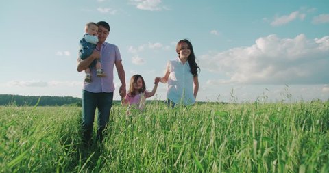 young happy Asian family goes on a green field with two children, slow motion Stockvideó