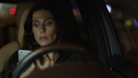 Attractive Smiling Business Woman Using Mobile Phone in a Car at Evening. Shot on RED Cinema Camera in 4K (UHD).