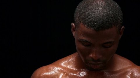 Footage.Wet naked Afro-American young man posing for photographer. Young man sweaty after hard gym training. Short haired man with muscular body isolated on black background. Fashion or vogue concept.